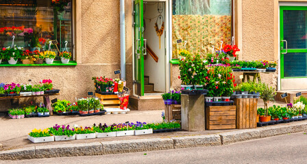 Fototapeta na wymiar Boxes with flowers and flowerpots on pavement in front of a flower shop. Cozy sidewalk of street in small Finnish town. Porvoo, Finland. External view of a florist store with display on pavement.