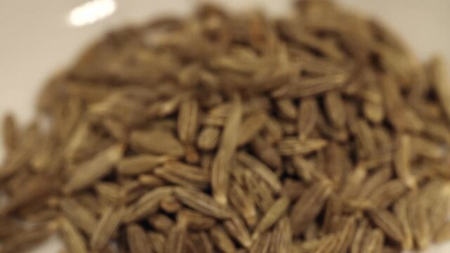 Macro close up of cumin seeds falling into a white bowl