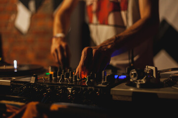 The hands of a DJ musician control the musical equipment in the bar