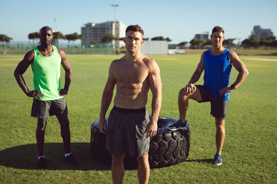 Portrait of diverse group of shirtless men exercising outdoors standing by tyre