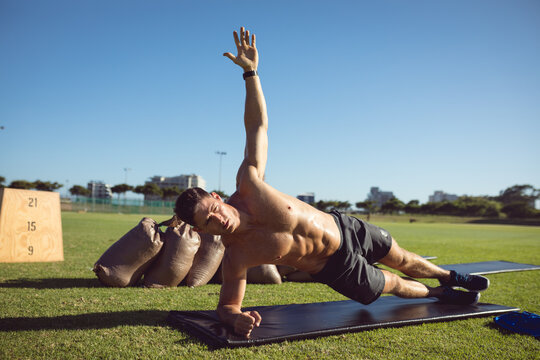 Caucasian muscular man exercising outdoors, doing side plank