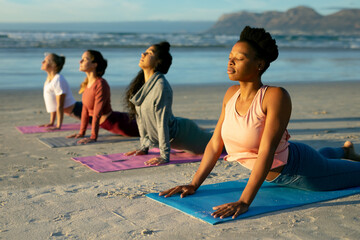 Group of diverse female friends practicing yoga, at the beach laying and starching with eyes close