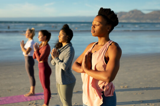 Group of diverse female friends practicing yoga, at the beach standing with eyes close