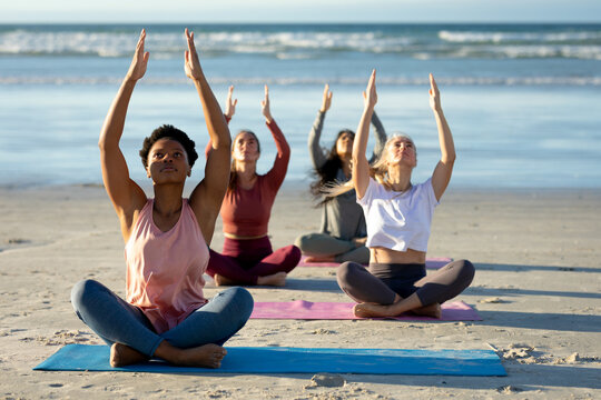 Group of diverse female friends practicing yoga, meditating at the beach