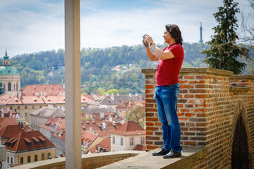 Fototapeta na wymiar A man stands on a brick wall and photographs the panorama of Prague. Journey