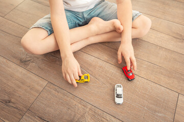 Little boy playing barefoot with toy cars on wooden floor in house