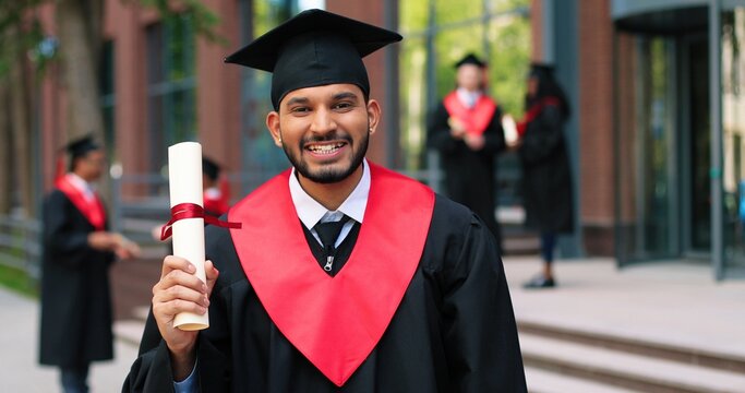 Young graduated boy holding his graduation degree convocation ceremony. Attractive multiracial student graduate posing towards the camera during the ceremony