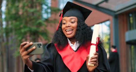 Portrait of a happy attractive multiracial graduate holding her smartphone and chatting via video...