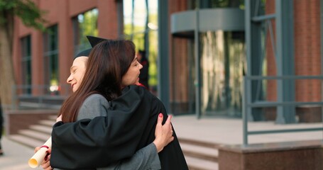 Happy mother and her student son on graduation day embracing with each other. Boy in academic gown and cap hugging his mother in front of the camera