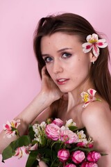 naked skinny girl holding flowers on a pink background. brunette