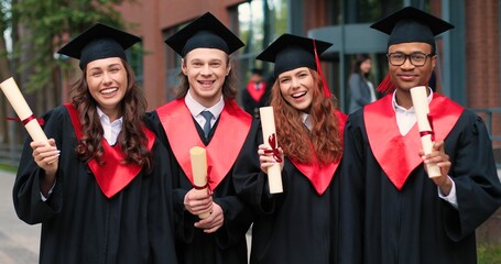 Unforgettable emotions. Waist up portrait of the group of students at the graduation gowns and caps standing near the university and sharing their emotions with each other