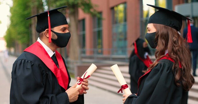 Waist up portrait view of the two students wearing protective masks greeting with elbows with each other and discussing their graduation during the covid 19 pandemic