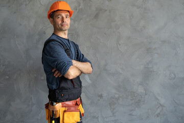 Laughing construction worker on the background of a gray concrete wall in a protective helmet with...