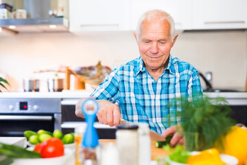 elderly man cuts vegetables for salad at the table in the kitchen