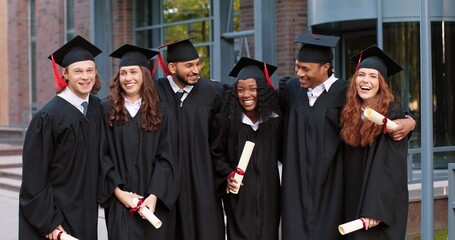 Company of happy multiracial student people are celebrating their graduation while standing near...