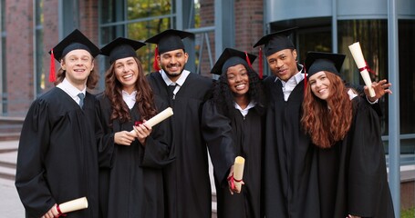 Company of happy multiracial student people are celebrating their graduation while standing near...