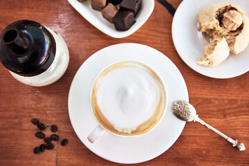 Cup of cappuccino on wooden table with cookie and chocolate.