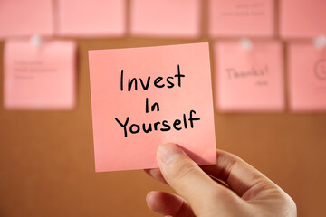Hand holding a sticky note text sign showing Invest In Yourself