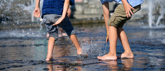 Little boys bare feet playing with fountain water jets at the square