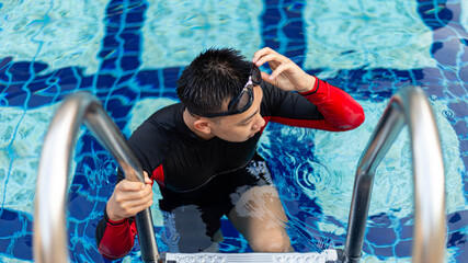 Sports and recreation concept a male adolescent wearing goggles and red and black swimming suit...
