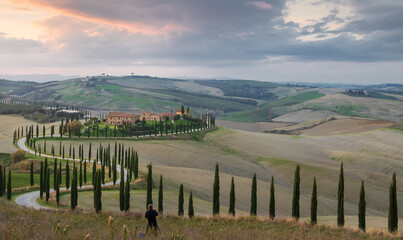 Fototapeta na wymiar photographer takes a photo of farm and road with cypress at sunset in Val d'Orcia. Tuscany. Italy