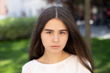 Fototapeta premium close-up of a young brunette girl with brown eyes and developing hair against background of green grass.