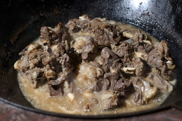 Asian and Uzbek cuisine, pieces of beef and lamb meat are stewed and fried in oil and in their own juice in a large black cauldron close-up, , cooking food
