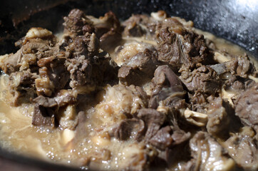 Asian and Uzbek cuisine, pieces of beef and lamb meat are stewed and fried in oil and in their own juice in a large black cauldron close-up, , cooking food

