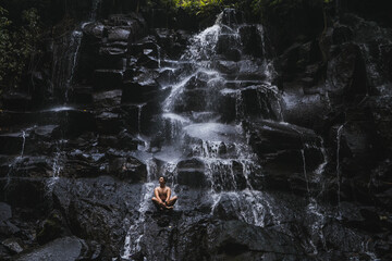 Young man sitting on the rock under the waterfall	