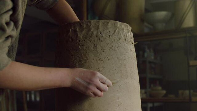 Beautiful clay vase is being scraped by a potter, modelling vessel's side on the rotating disk, working skillfully by her hands, pottery art, Close up, Slow motion.