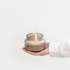 Woman hand holds lit scented candle in glass jar. Wellness and physical, emotional health concept.