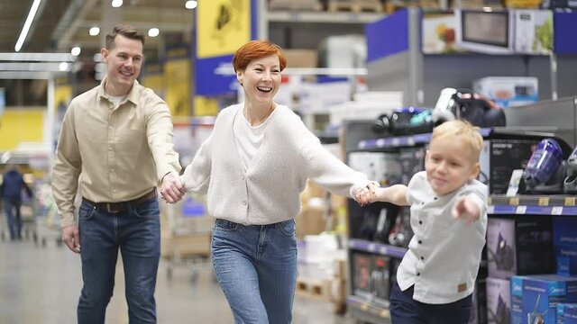 Excited family with kid son have fun in supermarket, running through aisles, making purchase. active enthusiastic parents spend weekends with son in store. Slow motion
