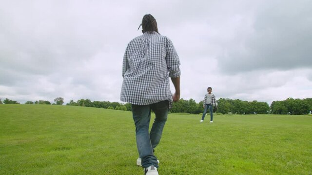 Joyful carefree handsome african american father with dreadlocks and excited cute school age boy with baseball glove, practicing baseball skills while enjoying leisure and having fun together in park.