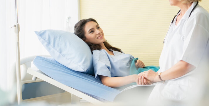 Hospitalized woman lying on the bed while a doctor examining woman patient in hosipal room.
