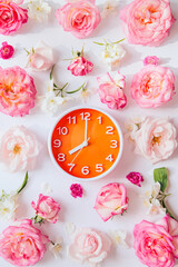 Orange round analog alarm clock on white background with rose buds. Summer morning concept. Eight o'clock. Top view. Flat lay.