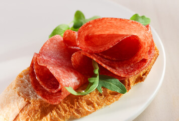 Brot mit Salami und Saltatblättern auf weissem Teller
