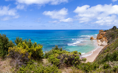 A picturesque landscape panorama of the Indian Ocean and the Great Australian Bay. View from the covered green bushes of the precipitous shore to the ocean sandy beach with rocky shores. Sunny day.