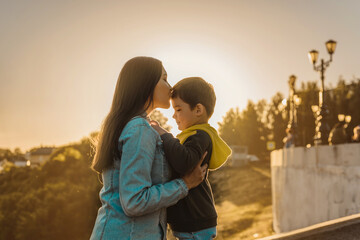 portrait of a happy young mother with a young son at sunset. the concept of happy motherhood, maternal parental love and care. mom kisses her son at sunset