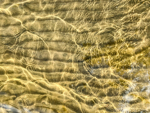 The textured sandy shallow bottom of the bay is close-up under a thin layer of water in sunny day. The gleams of water add even more structure to the sandbank.Abstract pattern in golden yellow. 