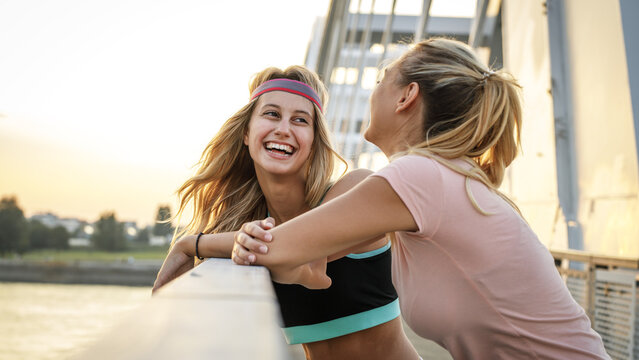Two best friends relaxing after jogging over the city bridge.Joying in sunset.	
