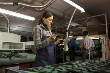 Concentrated young artisan holding leather pieces in shoemaking workshop. Female shoemaker working with material for new handmade footwear collection production. Shoe fabrication industry concept