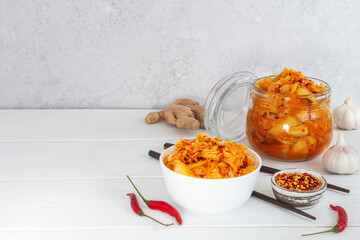 Probiotics fermented food kimchi cabbage in a glass jar and salad bowl with chopsticks on the white wooden background. Concept healthy vegetarian food. Great support the immune system. Asian cuisine.