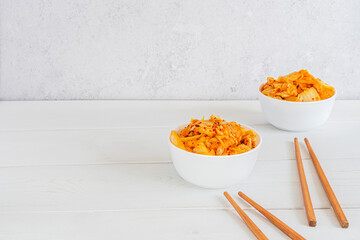 Probiotics fermented food kimchi cabbage in salad white bowls with chopsticks on the white wooden background. Korean food. Concept healthy vegetarian food. Horizontal orientation. Copy space.