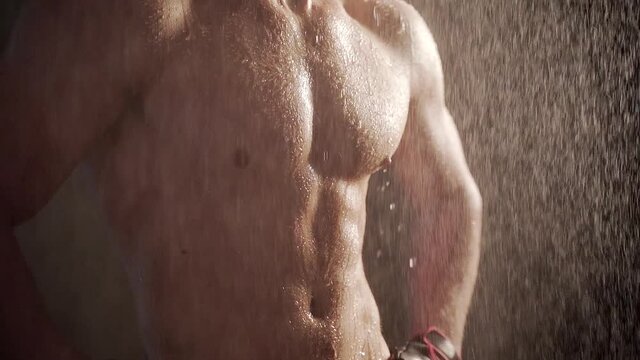 Close up body young man muscular guy bodybuilder on which water pours Portrait of Sexy Male Falling rain or shower on a dark background. Concept: sport, strong healthy body and motivation