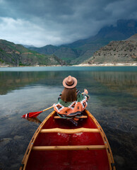 Obraz premium Girl canoeing on a lake in the mountains on a cloudy day. Moody atmosphere on Lake Gizhgit in the village of Bylym, Kabardino-Balkaria