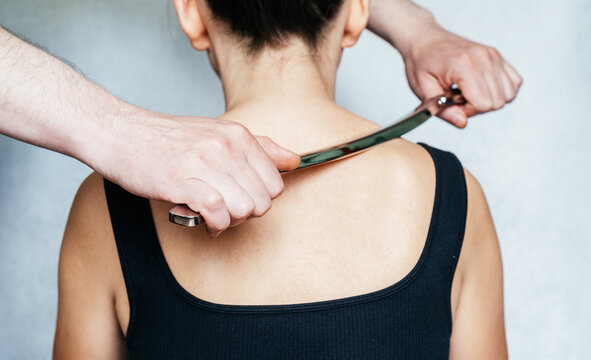 Osteopath practitioner performing fascia release maniupulations using IASTM treatment, a woman receiving soft tissue treatment on her neck with stainless steel tool
