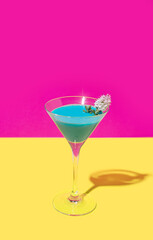 A attractive blue cocktail with a white flower against bright lovely magenta background and warm yellow bottom. Creative copy space.