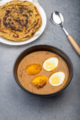 Fried egg curry or Anda Masala served in a bowl with  lachha parantha