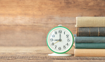 Back to school and education concept. The stack of books and alarm clock on the wooden background.
