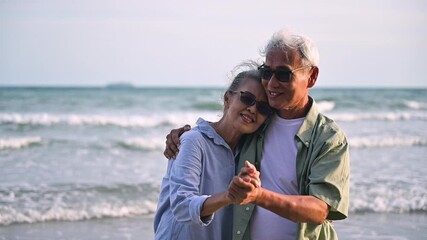 Asian senior couple tourist is hand in hands, embrace and dancing on tropical sea beach in summer holiday. Happy family couple elderly older retire resting relax together lifestyle on seaside outdoor.